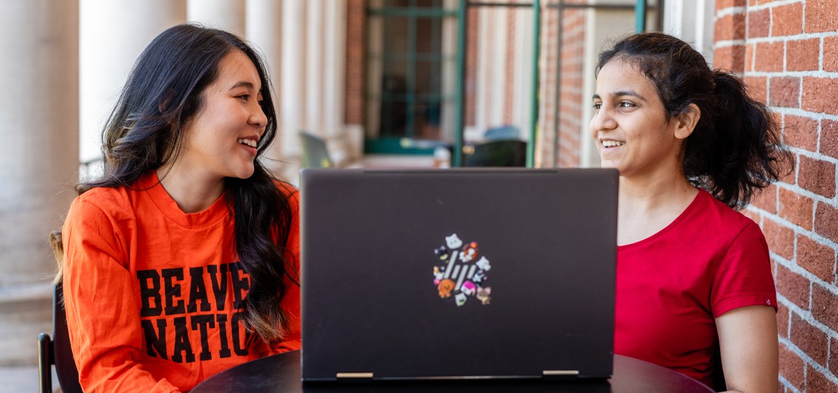 Two international students sitting together with a laptop